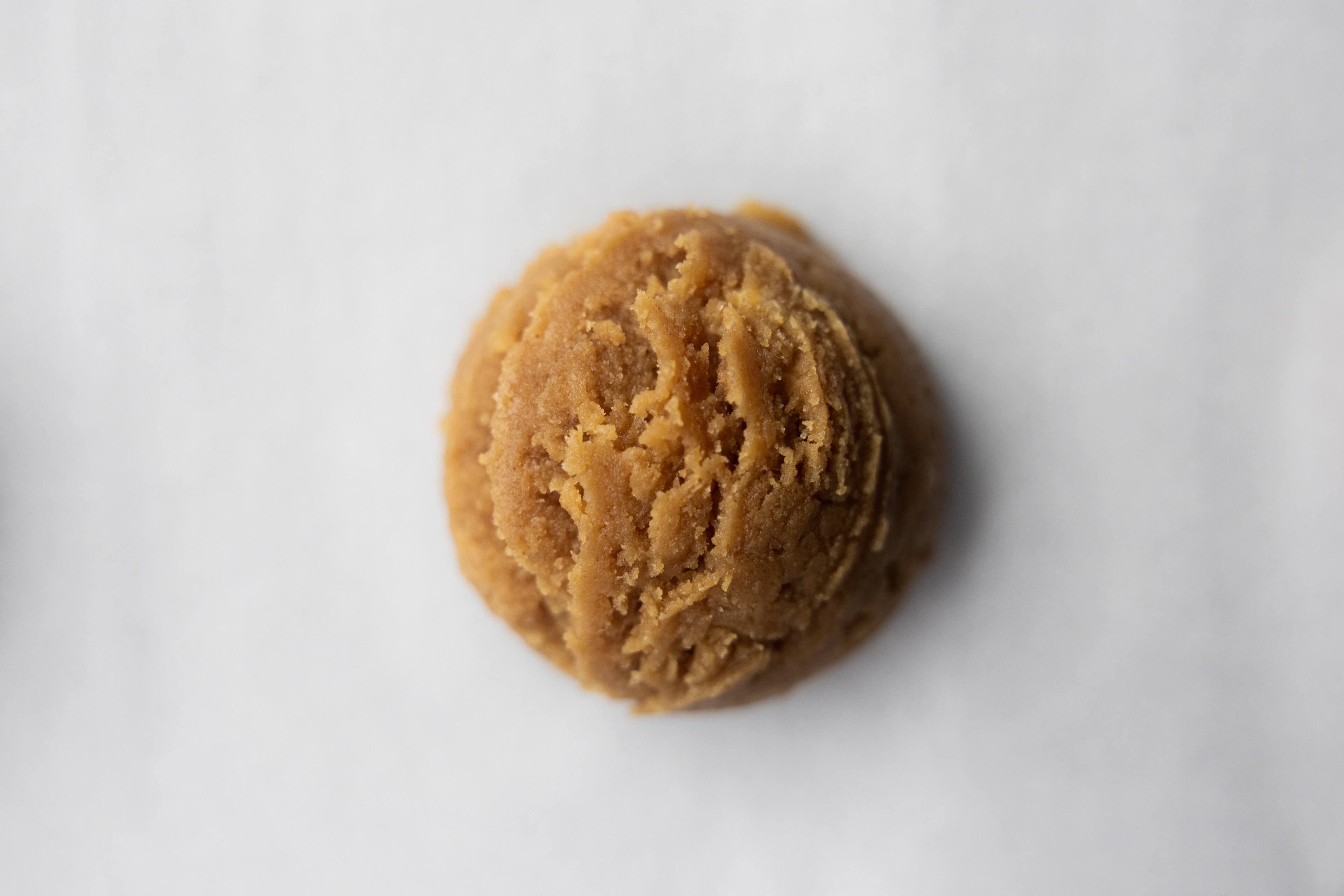 An overhead view of an open jar of creamy peanut butter with chopped peanut pieces, resting on a bed of raw shelled peanuts