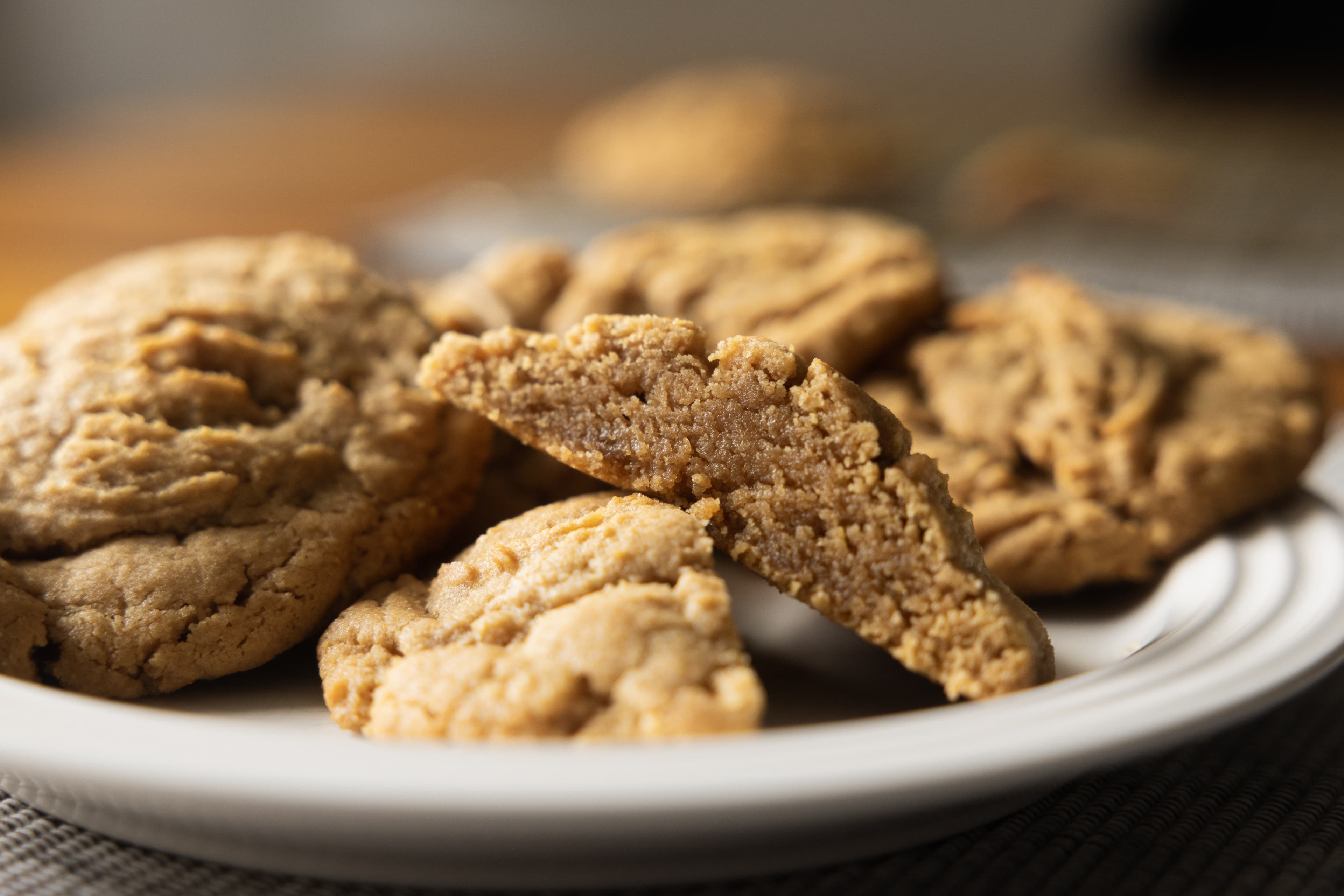 Golden peanut butter cookies on a plate with one split down the middle to show the thick centers.